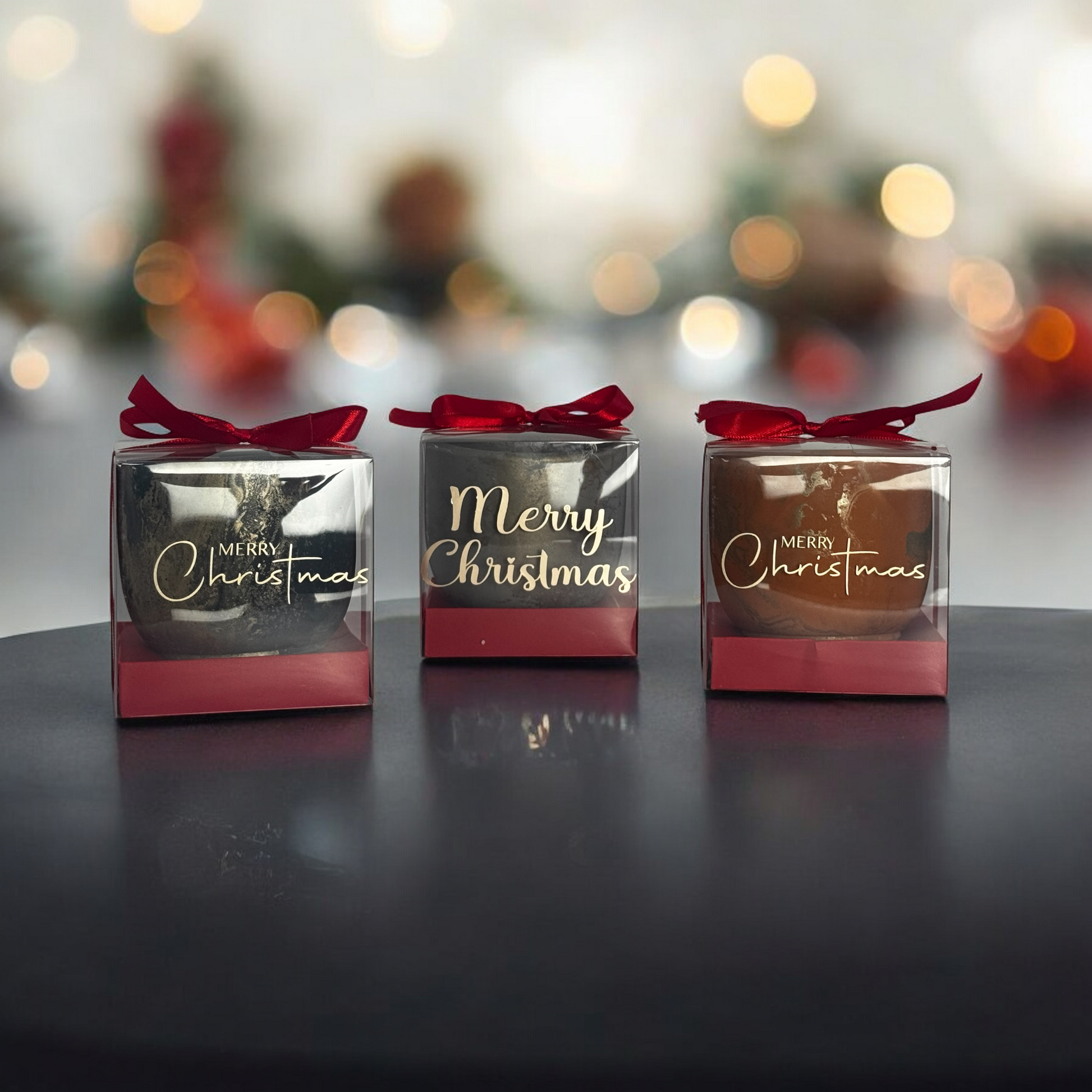 small Christmas gift boxes with red ribbons on a dark surface with blurred lights in the background.