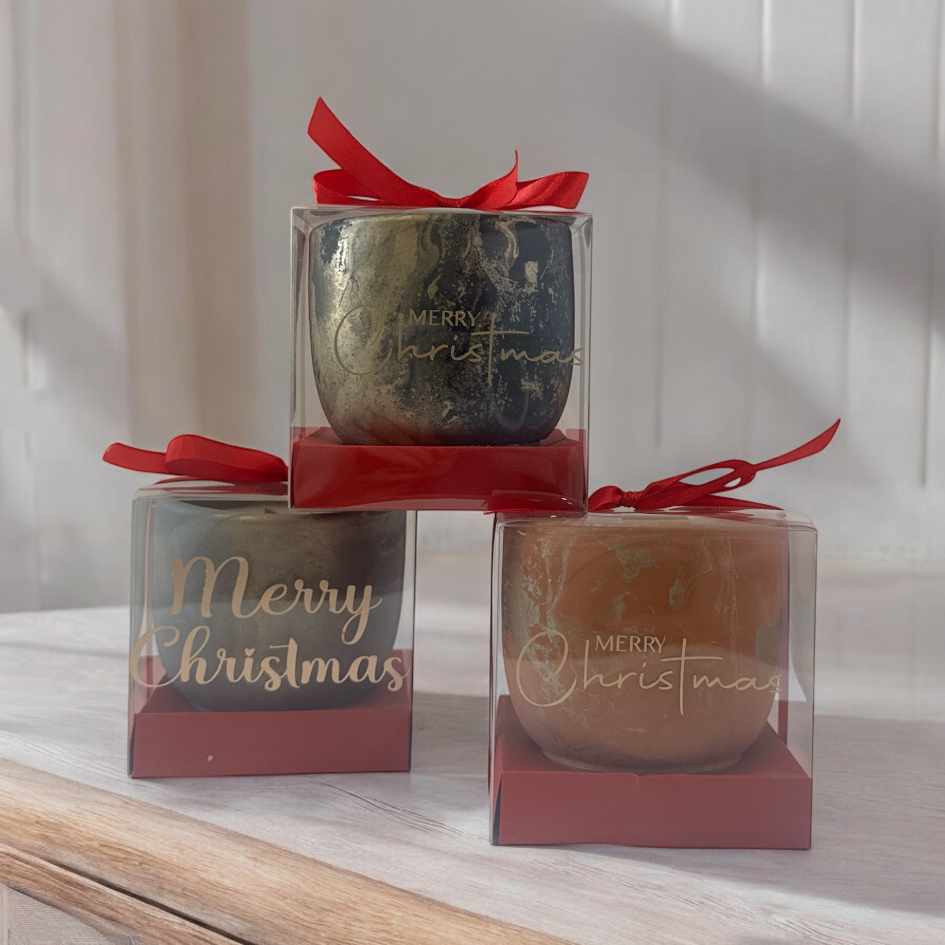  Christmas-themed candles in clear packaging with red ribbons on a light wooden surface.