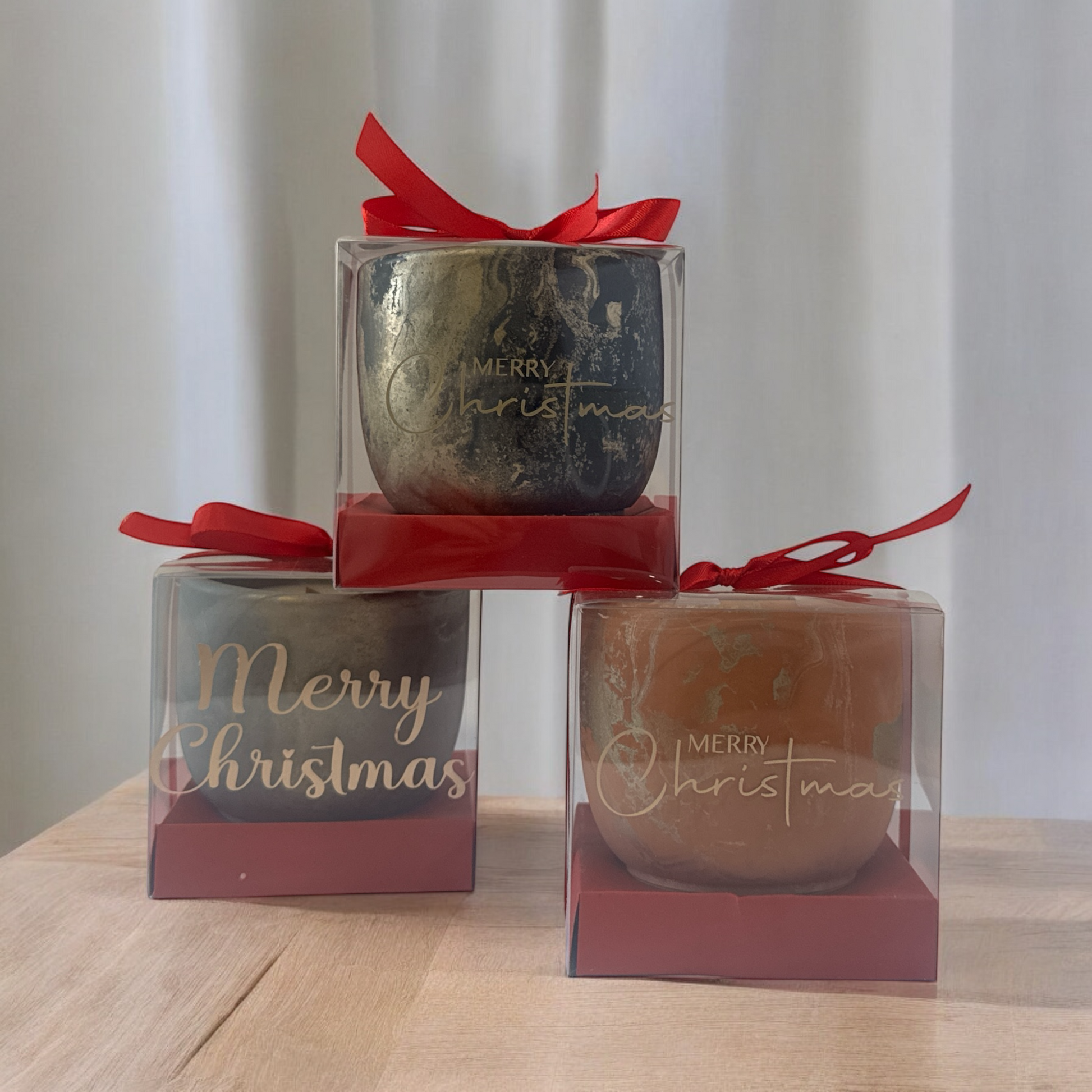 Handcrafted concrete Christmas candle in a clear gift box with red ribbon, luxury holiday soy candle by TAVV Home.Modern minimalist concrete soy candle packaged for Christmas gifting with festive décor around it.Set of luxury handcrafted concrete holiday candles with red bows, Christmas collection by TAVV Home.