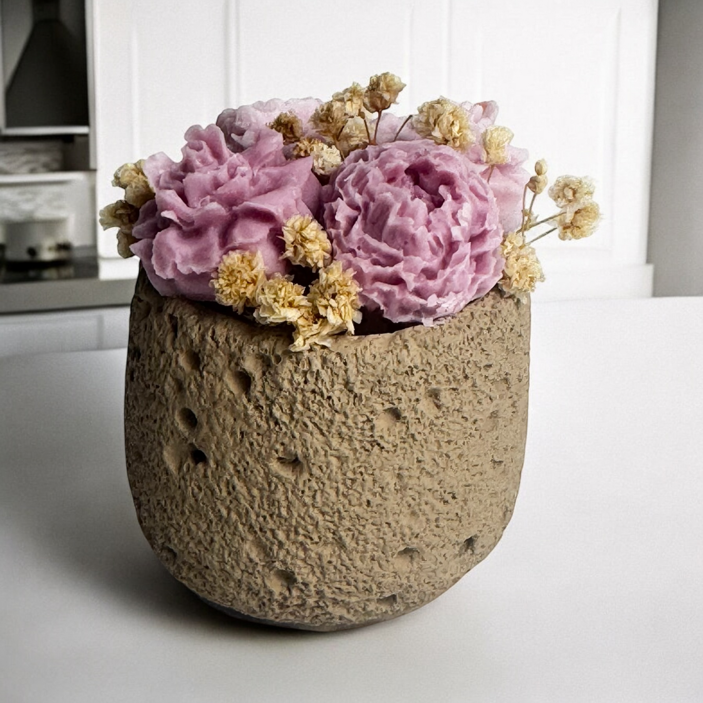 Blooming Candle with blush and lavender wax flowers, textured concrete container, handcrafted decorative piece.