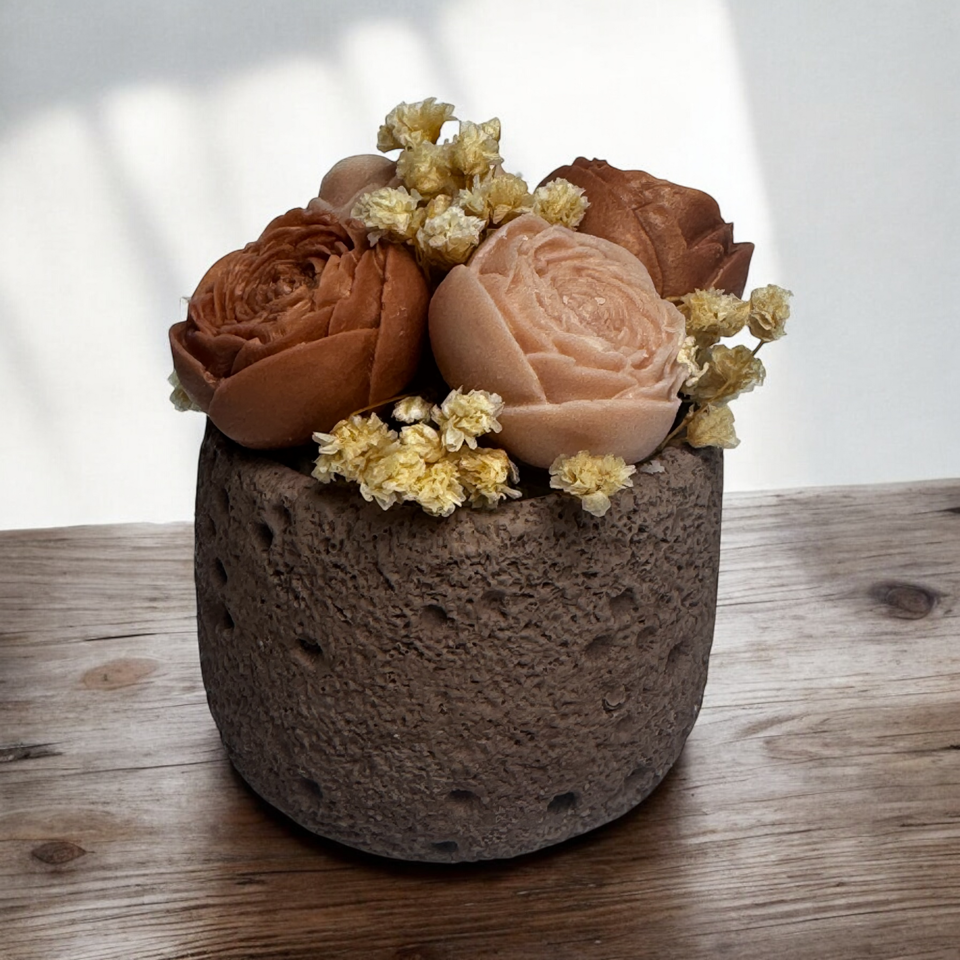 Decorative pot with brown and pink flowers candle on a wooden surface