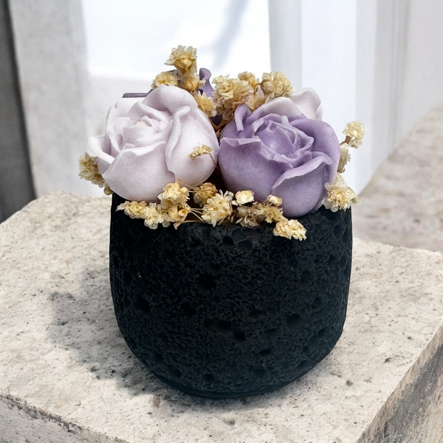 Black textured pot with purple and white flowers candles on a light surface
